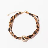 Gargantilla con doble tira de tela estampada animal print y dije de esfera dorada. Cierre con cadena dorada ajustable.