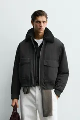 Cazadora bomber de corte cropped confeccionada en algodón, color negro. Presenta cuello de solapa con efecto borreguillo a contraste, cierre frontal con cremallera metálica, bolsillos delanteros tipo plastrón con solapa y acabados en rib en puños y bajo.