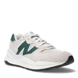 Championes urbanos New Balance modelo 57/40, con diseño en capas de gamuza beige y malla, destacando el logo N en color verde oscuro. Presentan una entresuela voluminosa y suela de goma negra.