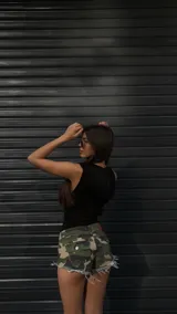 Short de jean con estampado de camuflaje en tonos verde, marrón y beige, con terminaciones desflecadas.