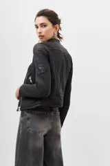 Campera de cuero ovino color negro, con cierre frontal asimétrico, cuello redondo con broche a presión y cierres metálicos en los puños.