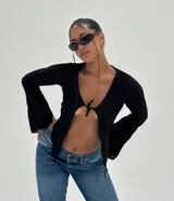 Top negro de tejido texturizado, manga larga acampanada y escote pronunciado que se ata con un nudo central, dejando el abdomen al descubierto.