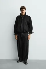 Cazadora cropped fit color verde militar, confeccionada en tejido efecto ante. Cuenta con cuello solapa, manga larga con puño abotonado, trabillas en los hombros, bolsillos laterales ocultos y un bolsillo interior. El bajo tiene elástico interior y el cierre frontal es con cremallera oculta por solapa con botones a presión.