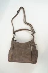 Bolso de hombro color marrón con acabado efecto cuero desgastado. Presenta dos bolsillos frontales verticales con cierre metálico, compartimentos laterales abiertos y una correa larga ajustable y extraíble.