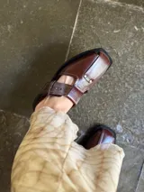 Sandalias tipo mule de cuero marrón con puntera cuadrada, diseño abierto y hebilla ajustable.