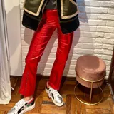 Pantalón rojo de cuero sintético con acabado brillante, de corte recto y detalle de tachas metálicas en los laterales de los tobillos.