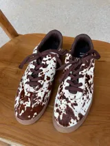 Championes urbanos con diseño de estampado animal print tipo vaca, confeccionados en cuero con textura de pelo. Presentan cordones marrones, suela de goma en tono tostado y detalles en color marrón oscuro en el cuello y lengüeta.
