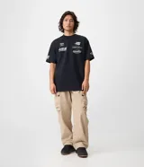 Remera de algodón color negro con corte relaxed, manga corta y cuello redondo. Presenta múltiples estampas localizadas con logotipos y textos de estilo automovilístico en el frente y las mangas.