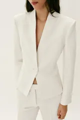 Blazer entallado color blanco de cuello sin solapa, manga larga con hombreras, falsos bolsillos delanteros de vivo y cierre frontal con un botón.