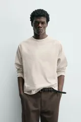 Camiseta de manga larga con cuello redondo, confeccionada en algodón compacto y pesado, con diseño de corte relajado y costuras decorativas en el cuello.