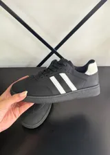 Championes estilo urbano color negro con dos franjas blancas laterales, detalle blanco en el talón, suela de goma texturizada y cordones negros.