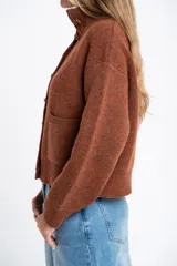 Cardigan de lana color marrón, con cuello alto, cierre frontal de botones y dos bolsillos delanteros. Presenta puños y ruedo acanalados.