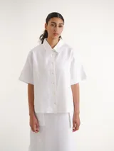 Camisa de manga corta blanca, con cuello camisero, cierre frontal de botones y diseño recto.