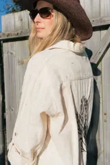 Túnica camisera de lino color beige, de corte largo y holgado, con mangas largas y bordado en la espalda con motivo de coral y texto.