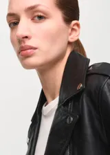 Chaqueta estilo biker de cuero negro, con cuello de solapa con muescas, cierre frontal cruzado con cremallera, bolsillos laterales con cremallera y un bolsillo pequeño con solapa y broche a presión.