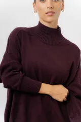 Sweater de tejido de punto color beige, con cuello alto, hombros caídos, mangas largas con puños acanalados y tajos laterales en el ruedo.