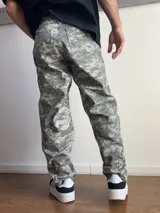 Pantalón de corte baggy con estampado de camuflaje digital en tonos grises y verdes. Presenta un diseño holgado y recto, ideal para un estilo urbano.