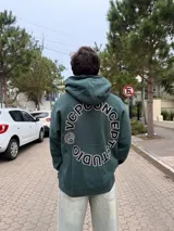 Buzo canguro oversize de color verde oscuro, con capucha y diseño gráfico circular estampado en la espalda con el texto VCP CONCEPT STUDIO.