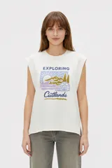 Musculosa color crudo con estampado frontal de paisaje montañoso y texto "EXPLORING Outlands", corte holgado y aberturas laterales en el ruedo.