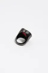 Anillo de metal con diseño en forma de corazón, acabado oscuro y detalle de esmalte rojo en el centro rodeado por un borde negro con letras grabadas.
