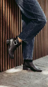 Bota corta de cuero color chocolate, con diseño minimalista, taco cuadrado de 4 cm y una hebilla metálica decorativa en el tobillo sobre una banda de gamuza.
