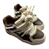 Championes urbanos de diseño robusto, combinando paneles de cuero y eco cuero en tonos marrón y blanco. Presentan cordones gruesos tipo soga, suela de plataforma con textura y detalles de marca grabados en el lateral.