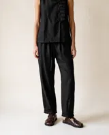 Pantalón de lino negro con silueta relajada y amplia, cintura elastizada con lazo de ajuste, bolsillos laterales y detalle de pequeños pliegues en la terminación del ruedo.