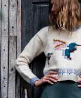Sweater de lana merino color natural tejido en punto jersey, con diseño jacquard multicolor de aves en el frente y detalles en tono celeste en cuello, puños y ruedo.