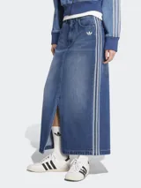 Falda larga de jean azul con corte recto y abertura frontal. Presenta tres tiras blancas verticales a los costados y logo de Adidas bordado en el frente.