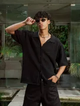 Camisa de manga corta color crudo/blanco, confeccionada en tejido de punto abierto con textura calada y cuello polo. Presenta cierre frontal de botones.