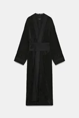 Kimono largo de manga larga con diseño abierto, confeccionado en tejido satinado negro. Presenta detalles de bordados florales a tono en el frente y en los puños, e incluye un cinturón tipo fajín ajustable con lazadas en la cintura.