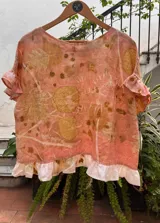 Top de lino con estampado botánico artesanal (ecoprint) en tonos rosados y ocres. Presenta mangas cortas con volados y un volado decorativo en el ruedo inferior en color blanco.