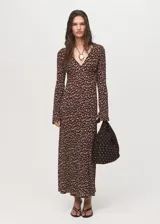 Vestido largo de corte evasé con estampado floral pequeño sobre fondo marrón. Presenta cuello en pico, mangas largas acampanadas y tejido plisado con caída fluida.