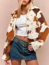 Chaqueta corta de textura tipo peluche con estampado animal print estilo vaca en tonos blanco y marrón. Presenta cuello alto, cierre frontal y corte oversize.