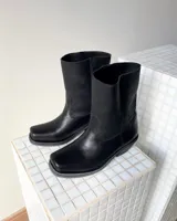 Botas de cuero vacuno color negro, con diseño versátil que incluye una polaina desmontable y un estribo decorativo con tachas metálicas. Presentan un taco bajo y punta redondeada.