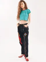 Pantalón de jean tiro alto tipo mom-fit con parches de colores en las piernas, apliques de tiento de cuero trenzado con canutillos alrededor de la cintura y costuras decorativas en zigzag.