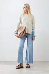 Sweater tejido color crema con diseño de trenzas, corte holgado y camisa celeste a rayas en los laterales.