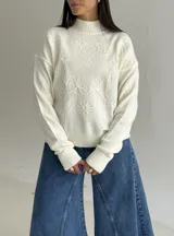 Sweater de punto color blanco con cuello polera, manga larga y diseño bordado al tono con motivos florales en el frente y las mangas.