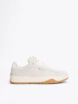 Zapatillas Tommy Jeans de corte bajo, color gris claro, confeccionadas en ante con interior de poliéster y suela de goma color caramelo. Presentan cordones blancos, logo de la marca en la lengüeta y etiqueta de Tommy Jeans en el lateral.