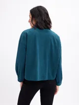 Campera de pana negra con cierre frontal de botones metálicos, cuello clásico y dos bolsillos frontales con solapa. Presenta mangas largas con puños abotonados y un diseño liviano sin forro.