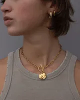 Collar de cadena de eslabones alargados con cierre frontal tipo T y dije circular de textura rústica e irregular.