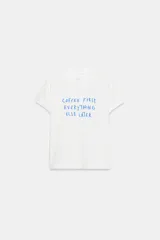 Camiseta blanca de algodón con cuello redondo, manga corta y estampado frontal con el texto en azul "COFFEE FIRST, EVERYTHING ELSE LATER".