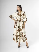 Vestido largo color crudo con estampado floral marrón, escote en V cruzado, mangas tres cuartos con volados y falda con niveles fruncidos.