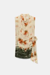 Vestido corto sin mangas de cuello redondo, con estampado tie-dye en tonos beige, naranja y verde oscuro. Presenta un lazo para atar en la cintura y cierre trasero con cremallera oculta.