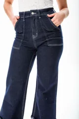 Pantalón de jean azul oscuro de corte ancho, con cintura alta, bolsillos delanteros y traseros con costuras blancas a contraste, y dobladillo ancho.