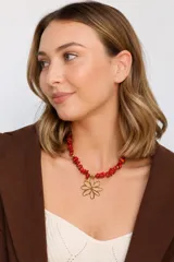 Collar de escallas de coral en tonos rojos con un dije colgante de flor en acero dorado.