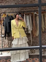 Blazer sastrero de lino en color amarillo pastel, con cierre frontal de un botón forrado, solapas clásicas y bolsillos laterales con solapa. Presenta un corte estructurado y forro interior de algodón.