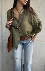 Camisa verde de tejido liviano, con cuello romántico con volados, mangas abullonadas tres cuartos con puños fruncidos y cierre frontal con botones.