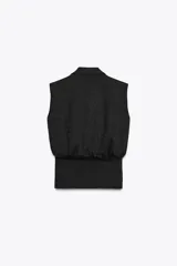 Top sin mangas confeccionado en tejido piqué, con escote cruzado tipo solapa y detalle de pliegues. Presenta una banda ancha ajustada en la cintura y un diseño de hombros caídos.