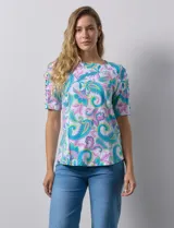 Remera de algodón estampado con diseño paisley en tonos celeste, rosa y amarillo. Tiene cuello redondo y mangas cortas con detalle de entrelazado y aberturas en los hombros.